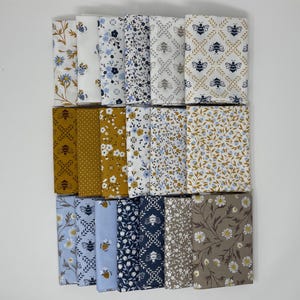 May include: A collection of folded fabric squares in various floral and bee patterns. Colors include white, blue, gold, and brown. The fabrics are arranged in a grid, showcasing the different designs.