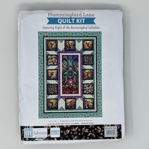 May include: Hummingbird Lane Quilt Kit featuring Flight of the Hummingbird Collection. The packaging displays a quilt design with a central rectangular panel surrounded by smaller square blocks in teal, purple, and black, measuring 56" x 76".