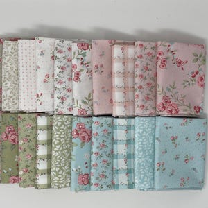 May include: A collection of folded fabric bundles in various floral and patterned designs. The fabrics feature pink, green, and blue hues with floral, polka dot, and plaid patterns. The bundles are arranged in neat rows, showcasing a variety of textile designs.