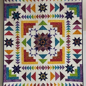 May include: A colorful, handmade quilt with a geometric star and triangle pattern. The quilt features a cream background with vibrant accents of purple, blue, green, yellow, and orange. The quilt is approximately 72 inches by 80 inches.