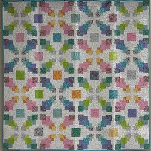 May include: A colorful quilt with a white background and a repeating pattern of squares and rectangles in shades of pink, green, blue, and yellow. The quilt has a teal border and is likely handmade.
