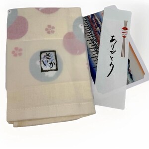 May include: Folded cream-colored cloth with pink and blue circular patterns and a small floral design. A square graphic with Japanese characters is visible. A white card with Japanese text and a decorative illustration is also present.