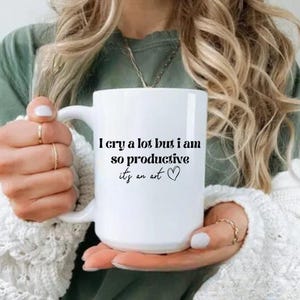 May include: White ceramic coffee mug with black text that reads "I cry a lot but I am so productive it's an art" with a small heart symbol.