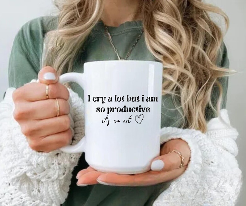 May include: White ceramic coffee mug with black text that reads "I cry a lot but I am so productive it's an art" with a small heart symbol.