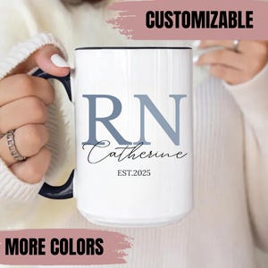 May include: White ceramic mug with a black handle and rim. The mug features the letters "RN" in blue, the name "Catherine" in script, and "EST.2025". The word "CUSTOMIZABLE" is at the top, and "MORE COLORS" is at the bottom.