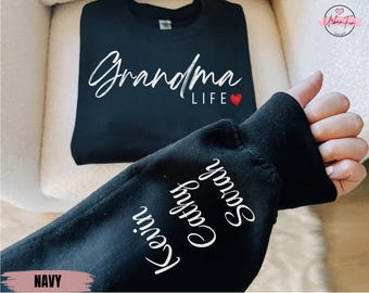 May include: A navy blue sweatshirt with the words "Grandma LIFE" in white script and a red heart. The sleeve displays the names "Kevin", "Cathy", and "Sarah" in white script. The word "NAVY" is at the bottom of the image.