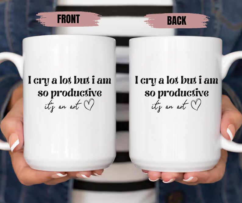 May include: Two white ceramic mugs with black text that reads "I cry a lot but I am so productive it's an art" and a small heart symbol. The mugs are held by hands.