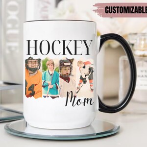 Puede incluir: Taza de cer&aacute;mica blanca con asa y borde negros. La taza presenta la palabra "HOCKEY" en letras negras grandes, con la palabra "Mom" debajo. La taza tiene cuatro fotos de ni&ntilde;os con equipo de hockey. La esquina superior derecha de la taza tiene la palabra "PERSONALIZABLE".
