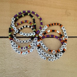 Peut inclure: Plusieurs bracelets de perles avec des phrases sur le thème d'Halloween. Les bracelets comportent des perles noires, orange, violettes et blanches épelant des phrases comme "Hocus Pocus", "Wicked" et "Just Here For The Boos".