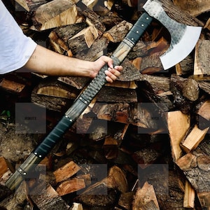 Op de afbeelding: Een strijdbijl met een lange steel en een grote, zilverkleurige metalen kop met een gehamerde textuur en een gebogen blad. De steel is gemaakt van donker hout met zwarte, met leer omwikkelde delen die zijn vastgezet met metalen klinknagels.
