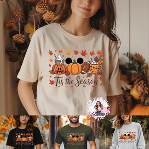 May include: Beige t-shirt with a fall-themed graphic. The design includes pumpkins, fall leaves, a football, and a coffee cup. The text "Tis the Season" is printed below the graphic. Additional shirts in black, green, and gray are shown.