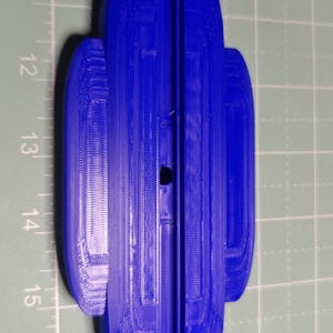 May include: A blue, 3D-printed object with a unique, symmetrical design. The object is approximately 6 inches long and features a central groove and rounded ends. The surface has a textured appearance, suggesting a layered printing process. The object is placed on a green cutting mat.