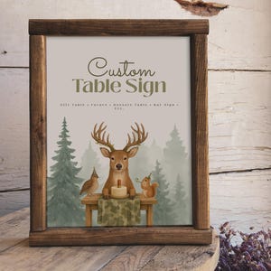 May include: A framed custom table sign with a rustic brown wooden frame. The sign features a watercolor illustration of a deer, bird, and squirrel around a table. The text "Custom Table Sign" is at the top.