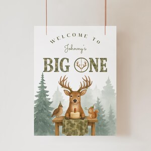 May include: A decorative sign with the text "WELCOME TO Johnny's BIG ONE." The sign features a deer with a birthday cake, a bird, and a squirrel. The background includes pine trees and a misty forest scene.