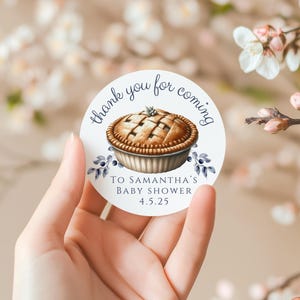 May include: A white round sticker with the text "Thank you for coming to Samantha's Baby Shower 4.5.25" and a watercolor illustration of a pie with a flaky crust and a lattice top.