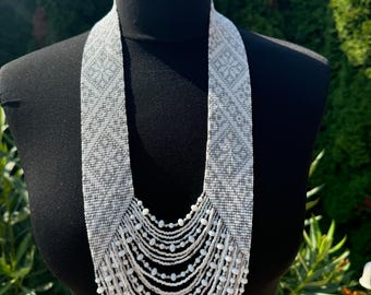 May include: A white beaded necklace with a geometric pattern. The necklace is made of small white beads and has a long, cascading design.