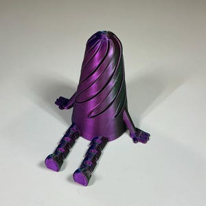 May include: A 3D-printed sculpture of a seated, abstract figure. The figure has a purple and green swirled body, small hands, and segmented legs. The legs and feet are a darker purple. The figure is sitting on a white surface.