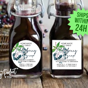 May include: Two glass bottles filled with dark purple elderberry syrup with white round labels that say "Home Made by Greg Elderberry Syrup" with a watercolor illustration of elderberries and leaves. The labels also list the ingredients: elderberry, water, honey, and cinnamon. The labels also list the recommended daily dosage for adults and children. The bottles are sitting on a wooden surface.