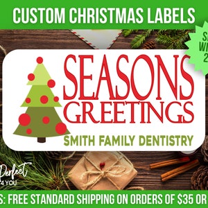 以下が含まれることがあります： 「Seasons Greetings」の赤い文字と、赤いオーナメントが付いた緑のクリスマスツリーが描かれた、カスタムクリスマスラベル。「Smith Family Dentistry」の文字が下にあります。木製の背景です。