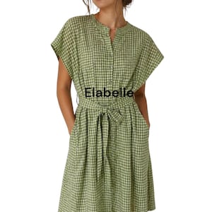 May include: A green and white checkered dress with short sleeves, a tie waist, and pockets. The dress has a button-down front and the word "Elabelle" is printed on the front. The dress is knee-length and made of a lightweight fabric.