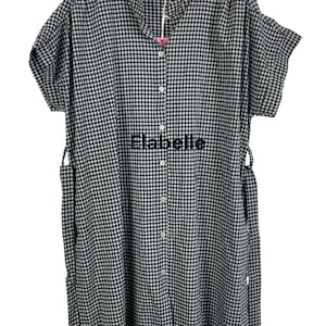 May include: A black and white gingham patterned dress with short sleeves and a button-down front. The dress has a mandarin collar and tie closures at the waist. The brand name "Elabelle" is printed on the front.