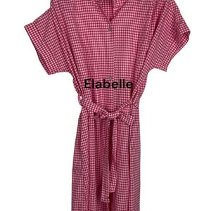 May include: A pink and white gingham dress with short sleeves and a matching belt. The dress has a button-down front and a mandarin collar. The text "Elabelle" is visible on the front of the dress.
