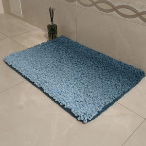 Op de afbeelding: Een rechthoekige badmat in ombre-stijl in blauwtinten. De mat heeft een zachte, getextureerde uitstraling, die overgaat van een lichter blauw naar een donkerder blauw. De mat ligt op een betegelde vloer. Ongeveer 70 cm x 50 cm.