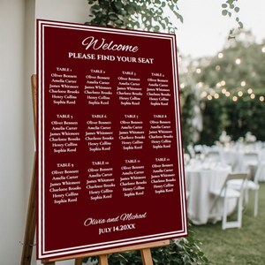 May include: A burgundy welcome sign with white text, listing guest names for tables 1-12. The sign reads "Welcome, PLEASE FIND YOUR SEAT" at the top, with the names of the couple and the date at the bottom. The sign is displayed on an easel.