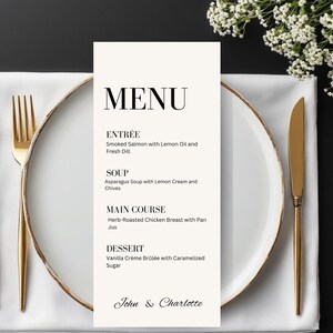 Könnte beinhalten: Eine formelle Menükarte mit dem Wort „MENU“ oben. Die Speisekarte listet Vorspeise, Suppe, Hauptgericht und Dessert-Optionen auf. Die Speisekarte befindet sich auf weißem Hintergrund, mit einem goldumrandeten Teller, goldenem Besteck und einer weißen Serviette. Der untere Teil der Speisekarte lautet „John & Charlotte“.