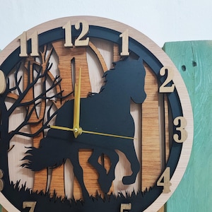 May include: A wooden clock with a black silhouette of a horse running through a forest. The clock face has Roman numeral hour markers and gold-colored hands.