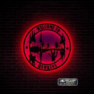 May include: A circular metal sign with a red neon glow against a brick wall. The sign reads "WELCOME TO HAWKINS" and features silhouettes of trees, bicycles, and a creature. Two stars flank the design. A small shipping graphic is in the lower right.