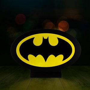 May include: A black and yellow Batman logo night light. The logo is in an oval shape and is illuminated from behind.