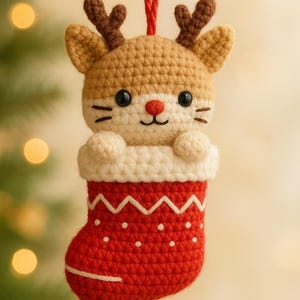 Op de afbeelding: Een handgemaakte gehaakte kerstversiering met een rendierkop die uit een rode kous komt. Het rendier heeft bruine geweien, zwarte ogen en een rode neus. De kous is rood met witte accenten en de tekst "PDF PATTERN".