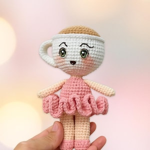 Peut inclure: Poupée au crochet en forme de tasse à café, vêtue d'une robe rose et d'un haut beige. La poupée a des yeux verts et un tutu rose. Le texte "PDF PATTERN" est affiché en haut.