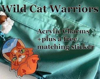 May include: An orange cat acrylic charm with a blue and white hat, attached to a keychain with a white pom-pom. The charm is in front of a teal background. Text reads "Wild Cat Warriors" and "Acrylic Charms + a free matching sticker."