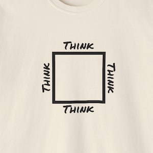 May include: A cream colored t-shirt with a black square outlined with a thick black line. The word "THINK" is written in black on each side of the square.
