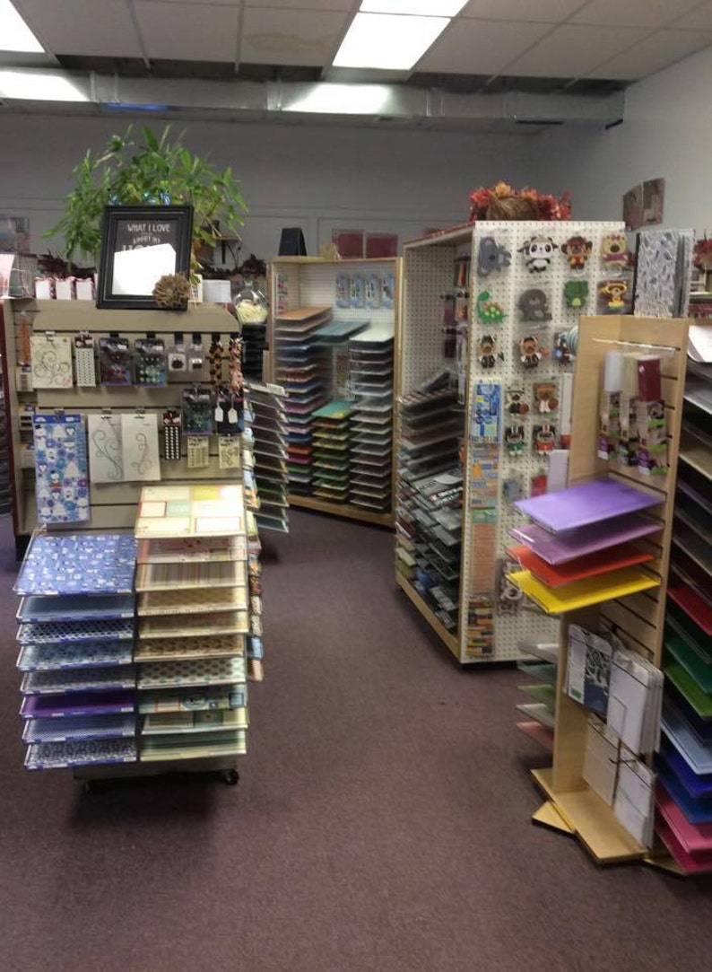 May include: A craft shop with shelves stocked with colourful paper, stickers, and other craft supplies. The shelves are arranged by colour and type of craft supply. The shop is well-lit and has a clean, organised appearance. The sign above the shelves reads "What I Love".