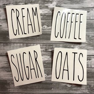 May include: Four white labels with black text on a wood background. The labels read "CREAM", "COFFEE", "SUGAR", and "OATS".