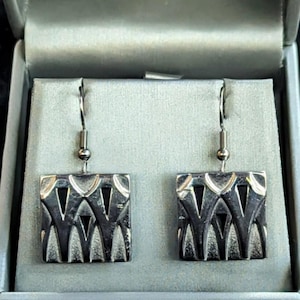 May include: A pair of silver dangle earrings with a geometric design. The earrings are square shaped with a cut-out pattern.