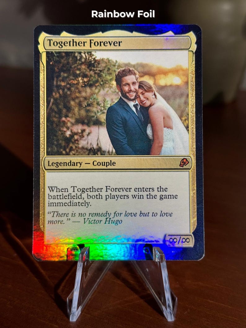 K&ouml;nnte beinhalten: Eine Regenbogen-Foil-Sammelkarte mit dem Titel Together Forever und einem Foto eines Paares in Hochzeitskleidung. Der Kartentext enth&auml;lt Legendary - Couple, Spielregeln und ein Zitat von Victor Hugo. Unten rechts sind Unendlichkeitssymbole zu sehen.