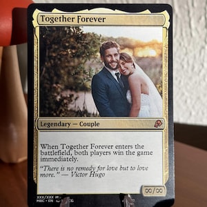 K&ouml;nnte beinhalten: Eine personalisierte Sammelkarte mit dem Titel Together Forever, die ein Foto eines Paares in Hochzeitskleidung zeigt. Der Kartentext lautet Legendary - Couple, enth&auml;lt Spielregeln und ein Zitat von Victor Hugo. Die St&auml;rke ist unendlich.