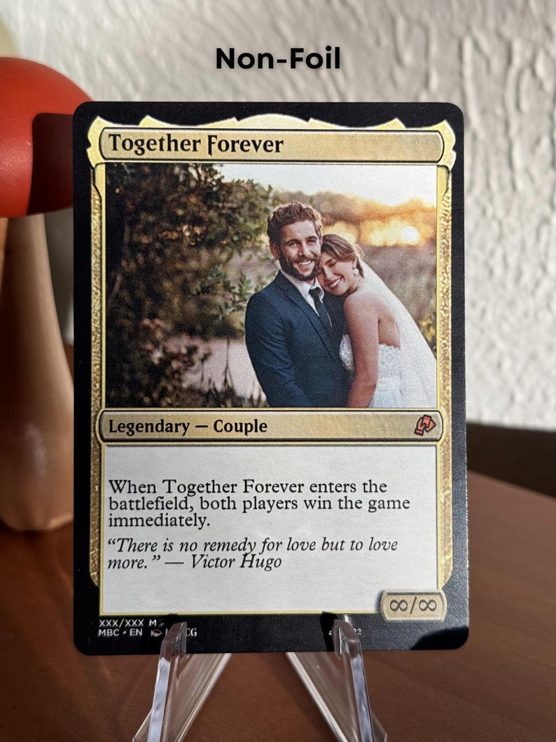 K&ouml;nnte beinhalten: Eine personalisierte Sammelkarte mit dem Titel Together Forever, die ein Foto eines Paares in Hochzeitskleidung zeigt. Der Kartentext lautet Legendary - Couple, enth&auml;lt Spielregeln und ein Zitat von Victor Hugo. Die St&auml;rke ist unendlich.