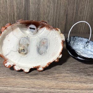 May include: A white ceramic figurine with a brown base. The figurine has a hole in the top and two holes on the bottom. The figurine is sitting on a wooden surface.