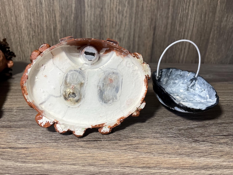 May include: A white ceramic figurine with a brown base. The figurine has a hole in the top and two holes on the bottom. The figurine is sitting on a wooden surface.