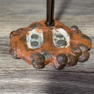 May include: A close-up of a brown and orange textured base with two circular indentations. Each indentation has two silver magnets inside.