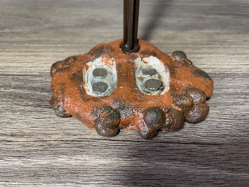 May include: A close-up of a brown and orange textured base with two circular indentations. Each indentation has two silver magnets inside.