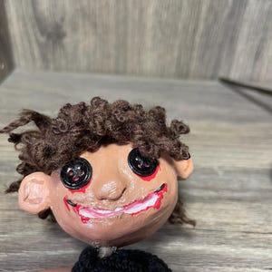 May include: Handmade doll with brown yarn hair, a painted face with red and black details, and a black knitted sweater.