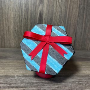 May include: A hexagonal gift box with a blue and black striped pattern and a red ribbon tied in a bow.
