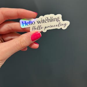 Puede incluir: Una pegatina holográfica con el texto "Hello witchling Hello prince ling" en forma de nube blanca.