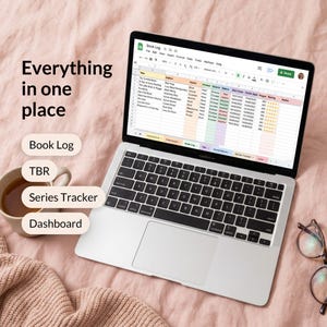 May include: A silver laptop displaying a digital book log spreadsheet with columns for title, author, genre, and rating. Text on the left reads: Everything in one place, Book Log, TBR, Series Tracker, and Dashboard. A mug and glasses are nearby.